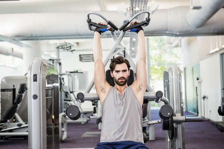 Focused man using weights machine for arms at the gym