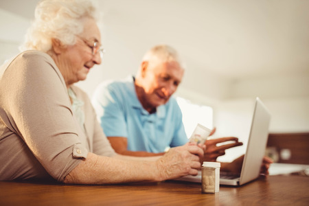 Senior couple using laptop and holding pills at homeの写真素材