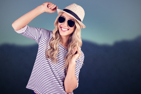 Gorgeous smiling blonde hipster posing with straw hat against blurred mountainsの写真素材
