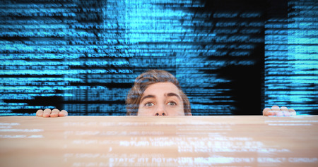 Man hiding behind desk against white background against shiny blue coding on black background