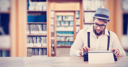 Hipster wearing eye glasses and hat working on typewriter against library
