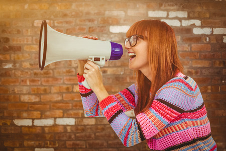 Smiling hipster woman shooting through megaphone against brick wallの写真素材