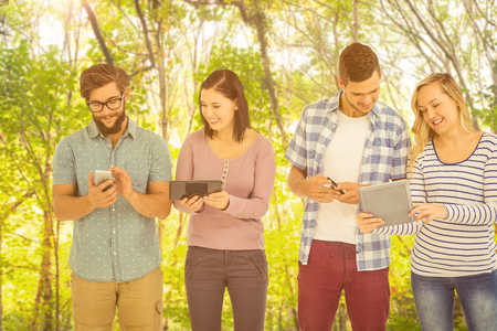 Smiling business people using electronic gadgetsagainst green forestの写真素材
