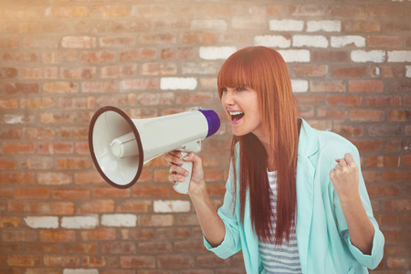 Hipster woman shooting through megaphone against brick wallの写真素材