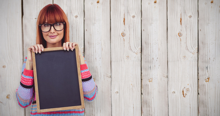 Smiling hipster woman holding blackboard against wooden backgroundの写真素材