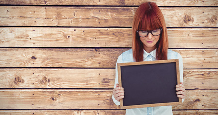 Smiling hipster woman holding blackboard against wooden planks backgroundの写真素材