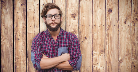 Confident hipster wearing eye glasses with arms crossed against wooden planks backgroundの写真素材