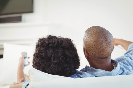 Rear view of couple watching television on the sofaの写真素材
