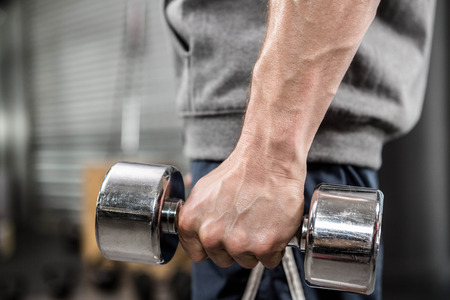 Muscular man with grey jumper holding dumbbell at the crossfit gymの写真素材