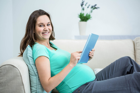 Pregnant woman using tablet on couchの写真素材