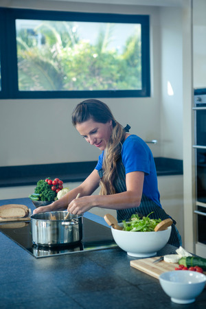smiling woman cooking vegtables in a saucepan on a stove topの写真素材