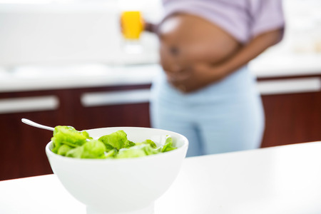 Pregnant woman in kitchen with salad on table at home