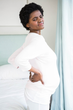 Pregnant woman with back pain in bedroomの写真素材