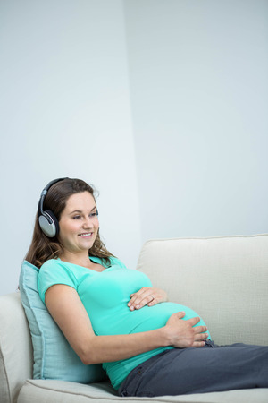Pregnant woman listening to music on couchの写真素材