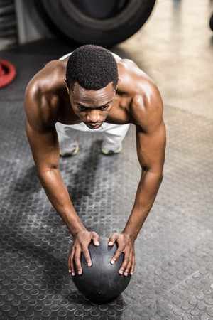 Muscular man doing push up with medicine ball at the crossfit gym