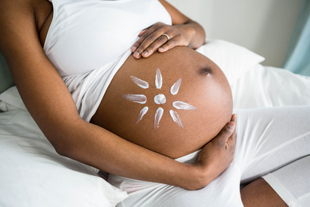 Pregnant woman applying cream on her belly at home