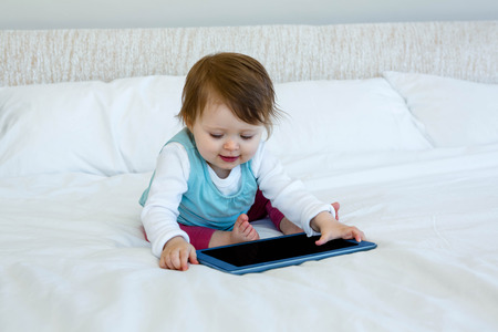smiling baby playing with a tablet on a bed