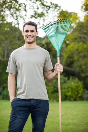 Portrait of young man standing with a gardening rake in garden