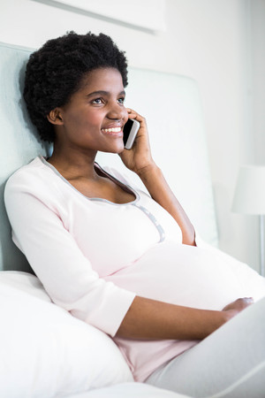 Pregnant woman on the phone on bedの写真素材