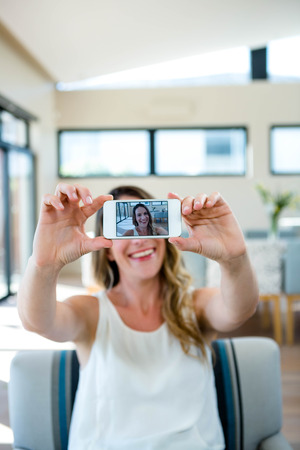 smiling woman sitting on a couch taking a selfieの写真素材