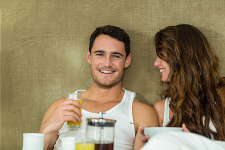 Young couple having breakfast on bed in bedroomの写真素材