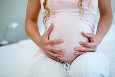 pregnant woman, sitting on her bed, holding her bump