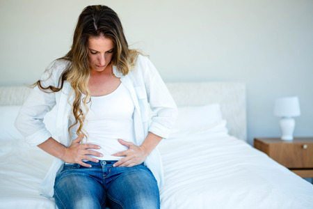 woman sitting on her bed holding her stomach in discomfortの写真素材