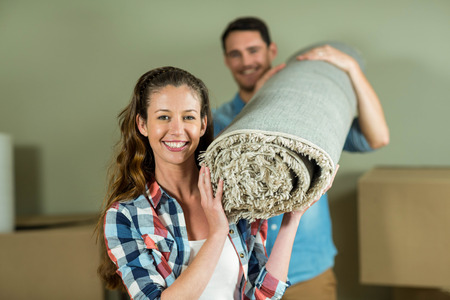 Happy couple carrying rolled up rug in their new houseの写真素材