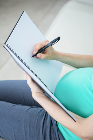 Pregnant woman writing on document on couchの写真素材