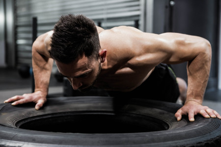 Shirtless man doing push ups on heavy tire at the crossfit gymの写真素材