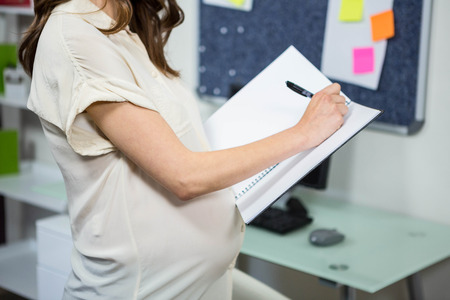 Pregnant businesswoman writing in folder in home officeの写真素材