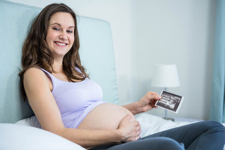 Pregnant woman showing ultrasound scan on bed