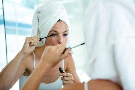 woman wearing a towel on her hair applying mascaraの写真素材