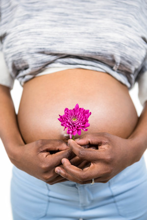 Pregnant woman with flower touching her belly on white backgroundの写真素材