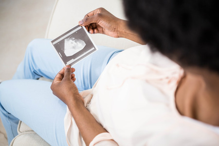 Pregnant woman holding ultrasound scan on couchの写真素材