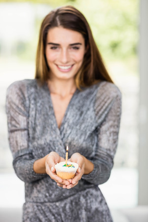 Portrait of beautiful woman holding birthday cupcake with one candle