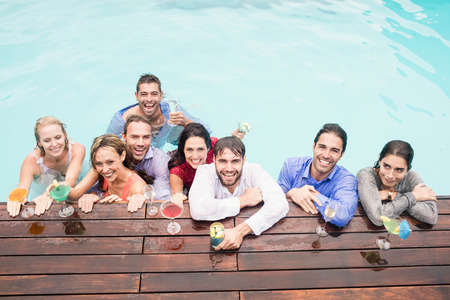 Happy young friends having drinks at swimming pool enjoying holidayの写真素材
