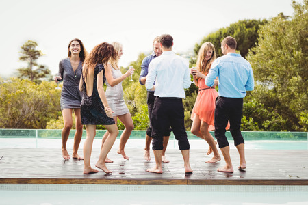 Happy young friends having drinks at swimming pool and enjoying holidayの写真素材