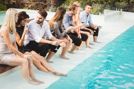 Young people sitting by swimming pool, drinking, having fun, enjoying holiday