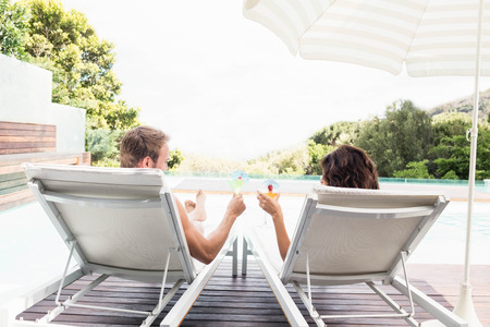 Young couple sitting on sun loungers by swimming poolの写真素材