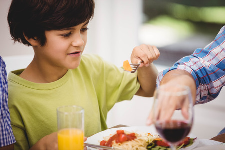 Boy holding a fork while having a meal at dining tableの写真素材