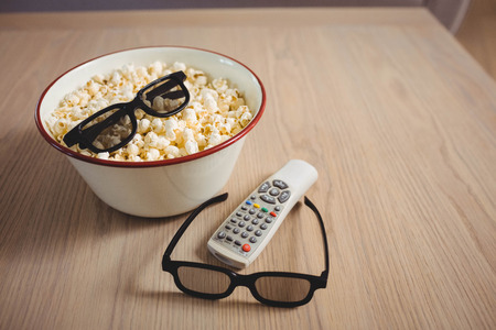 Bowl of popcorn, 3D glasses and television remote on table in living room