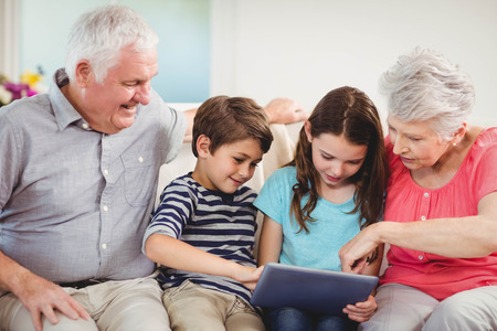 Senior couple and their grand children using digital tablet in living room