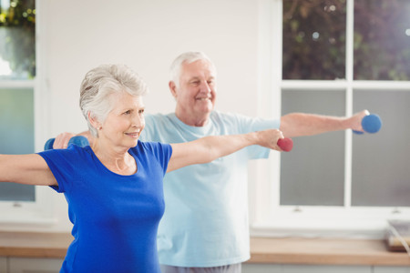 Senior couple performing stretching exercise with dumbbells at homeの写真素材