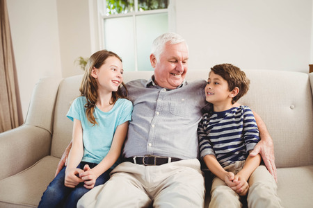 Grandfather and grandchildren sitting together on sofa in living roomの写真素材