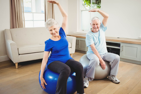 Senior couple doing stretching exercise on exercise ball at homeの写真素材