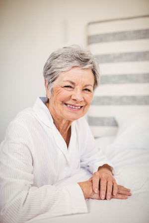 Portrait of happy senior woman sitting on bed in bedroom