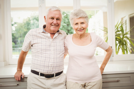 Portrait of senior couple smiling and standing in kitchen at homeの写真素材