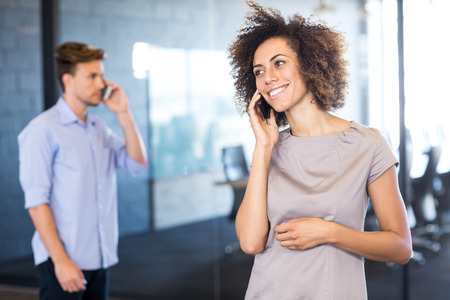 Colleagues communicating on mobile phone in front of conference room in officeの写真素材