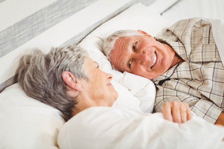 Happy senior couple laughing in bed in bedroomの写真素材